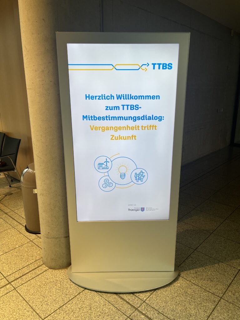 Innovative digital Anzeigetafel für TTBS Thüringen, begrüßt Besucher zum Mitbestimmungsdialog.
