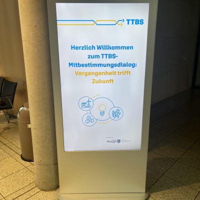 Innovative digital Anzeigetafel für TTBS Thüringen, begrüßt Besucher zum Mitbestimmungsdialog.
